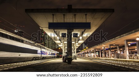 Nocturnal view of a train station. A man looks at his smartphone