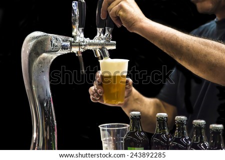 Man drawing beer from tap in an plastic cup. Isolated in a black background