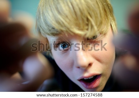 A blond teen boy with an interesting expression looking like he is reaching into the camera.