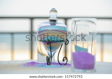 The container and aftermath from the unity sand ceremony performed in front of a beach.  Colorful sand using purple, aqua, and gold colors.