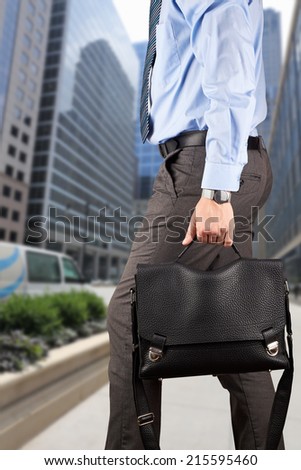 Businessman walking and holding  a  leather briefcase in his handss Modern city behind