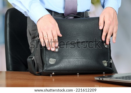 Businessman  standing closing  a  leather briefcase. Office area behind