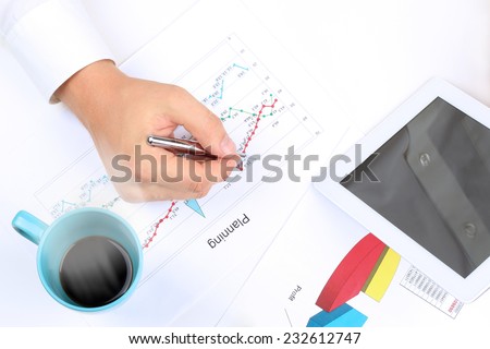 young businessman working in the office,  sitting at his desk, analyzing  data in  graphics, hot coffee behind