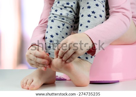 Children\'s legs hanging down from a chamber-pot on a green background
