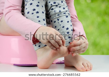 Children\'s legs hanging down from a chamber-pot on a green background