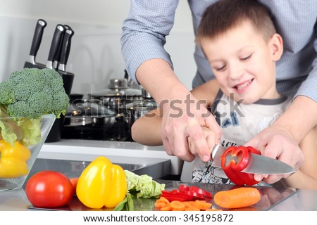 food, family, cooking and people concept - Man chopping paprika on cutting board with knife in kitchen with son
