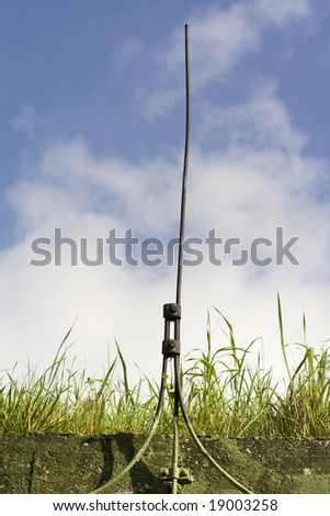 Lightning conductor on top of underground munition bunker with grass on roof against blue sky