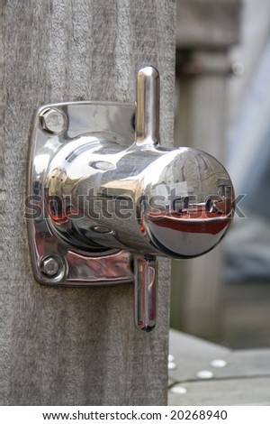 Shiny metal bollard on hardwood mooring pole reflecting horn of tourist boat in canal of Bruges