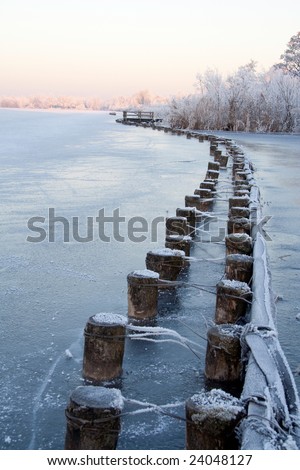 Pole and facing protecting shore of frozen lake on a winter morning