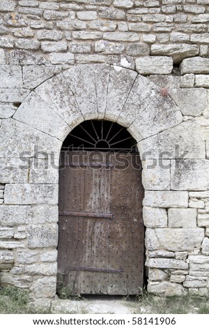 Very old wooden door reinforced with nails in arched stone door-frame