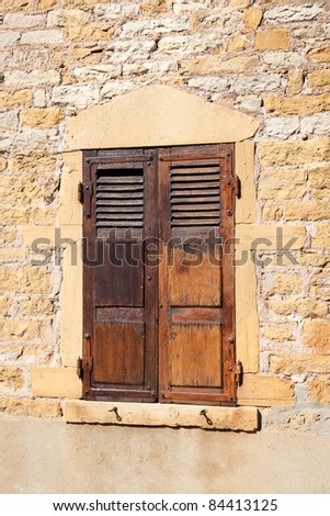 Closed wooden shutters in a window frame of a very old house built from yellow rocks in the village of Oignt, Beaujolais region, France