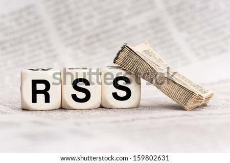 wooden dice depicting the letters RSS, with a stack of newspapers leaning on a dice