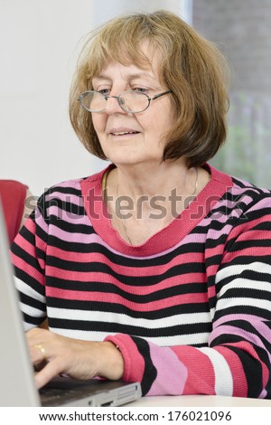 A lady wearing a striped shirt and glasses typing on a laptop.