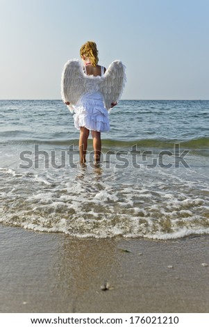 A young girl with angel wings on standing in the water at the beach.