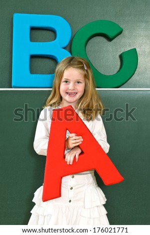 A young blonde haired girl hold a large letter A in her hand.