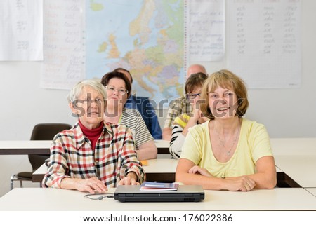 Four old women and two man sitting in a classroom.
