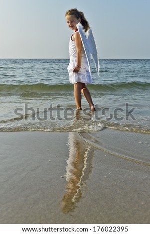 A young girl with angel wings wades in the water.