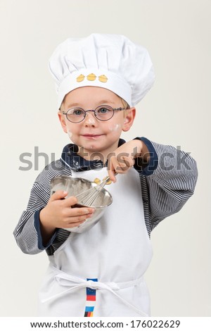 A young boy wearing a chef\'s hat is whisking in a bowl.