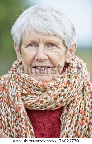 An older woman wearing a knitted scarf and a red sweater.