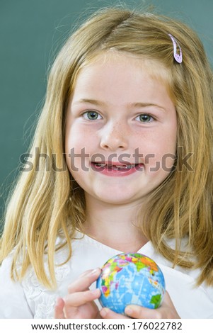 A girl with freckles smiles and holds a small globe.