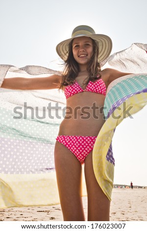 A young girl in a pink bikini with her towel blowing in the wind.