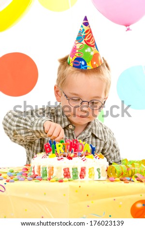 A small boy in a plaid shirt reaching towards a candy covered birthday cake.
