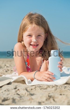 A girl lying on the beach with a lotion in her hands.