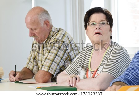 An old man writes while a woman stares at something.