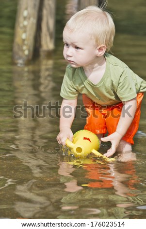 Toddler boy playing in water with a toy.
