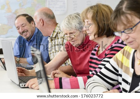 An elderly group sitting in a line looking at three different laptops in classroom.