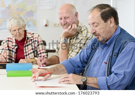 Two older men and one woman sitting at a table taking notes.
