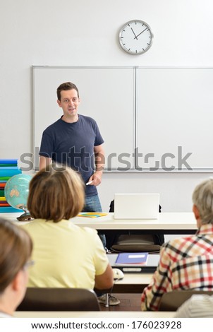 A teacher lectures a class of children in front of a white board.