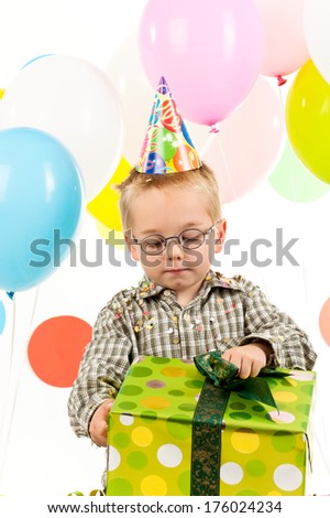 A little boy in a party hat opening a big gift box.