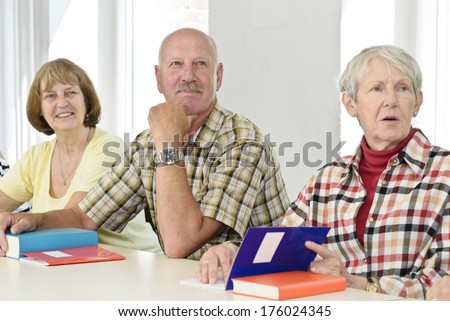 A group of elderly people at a table with books.
