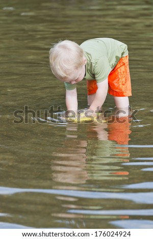A young boy with bright orange pants plays in the water.