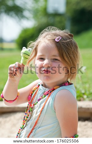 A girl with a frog finger puppet on her finger.