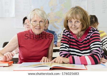 Two older women looking at the camera with a book.
