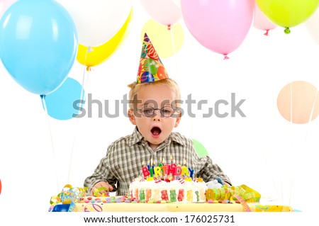 A young boy with a party hat about to blow the candles.