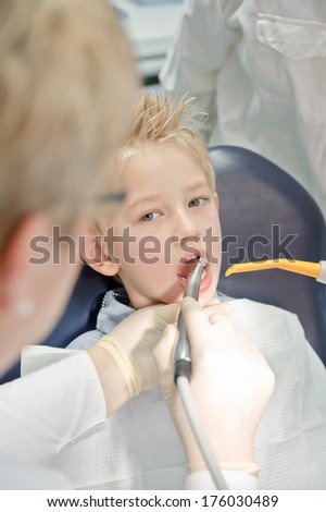 A boy sitting in a dentist chair while a dentist polishes his teeth.