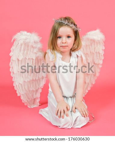 A girl kneeling and wearing angel wings and a halo.
