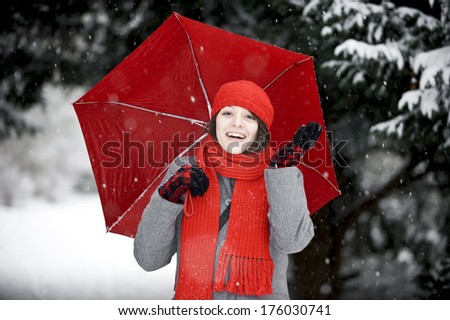 A woman with a red hat and scarf holding a red umbrella in the snow.