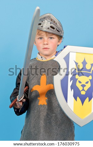 A little boy wearing a knight\'s costume and holding a sword and shield.