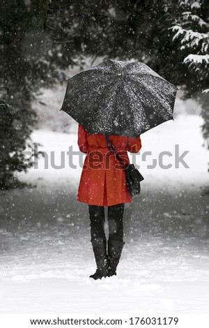 A woman wearing a red coat and holding a black umbrella on a snowy day.