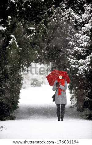 A woman stands outside with an umbrella while it snows.