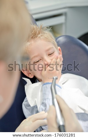 A boy holding his hand over his mouth while sitting in a dentist chair.