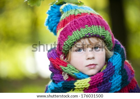 Young blond boy wearing a scarf and a bonnet with multiple colors.