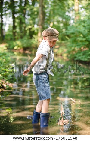 A little boy wading in water with rubber boots.