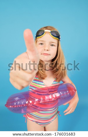 A little girl in swim gear giving a thumbs up.