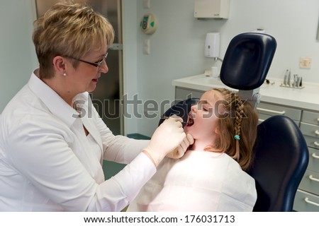 A dentist looks inside a girl\'s mouth with an instrument.