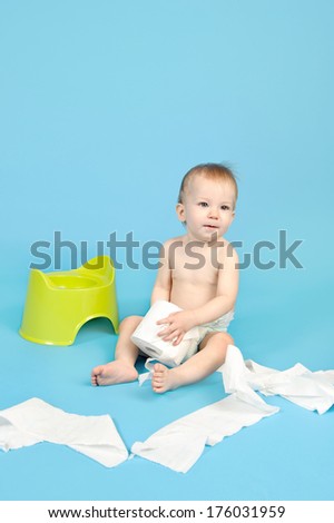 A baby sitting on the floor by a training potty with toilet paper unraveled.
